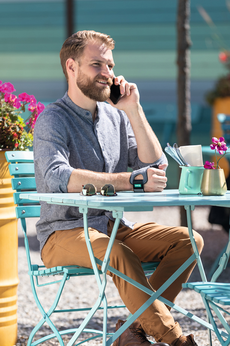 JuzoPro Rhizo Xtec Soft A man wearing a thumb brace is sitting in a café