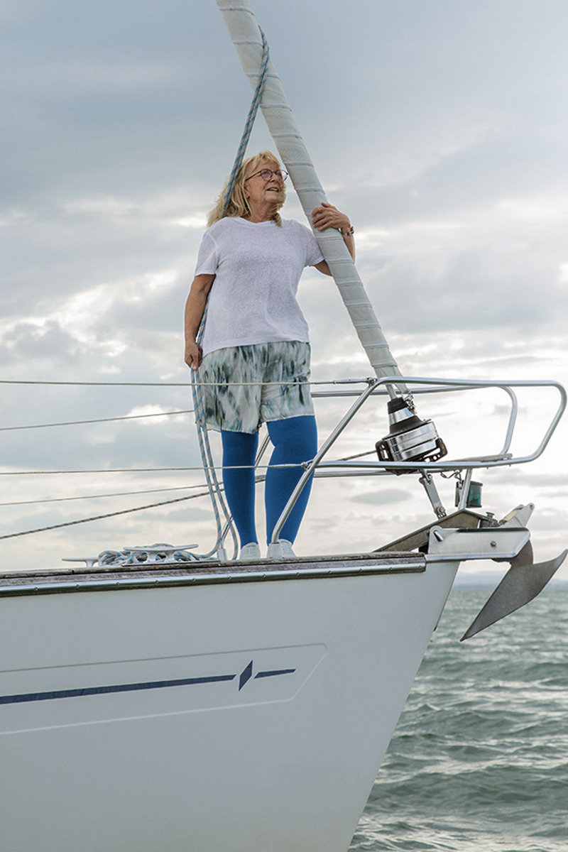 A woman is standing on a boat. She has lymphoedema in her leg and is wearing blue compression stockings A woman is standing on a boat. She has lymphoedema in her leg and is wearing blue compression stockings