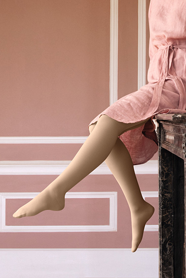 2. Lifestyle image Juzo Soft Woman with Juzo Soft Sesame sitting on a mantelpiece