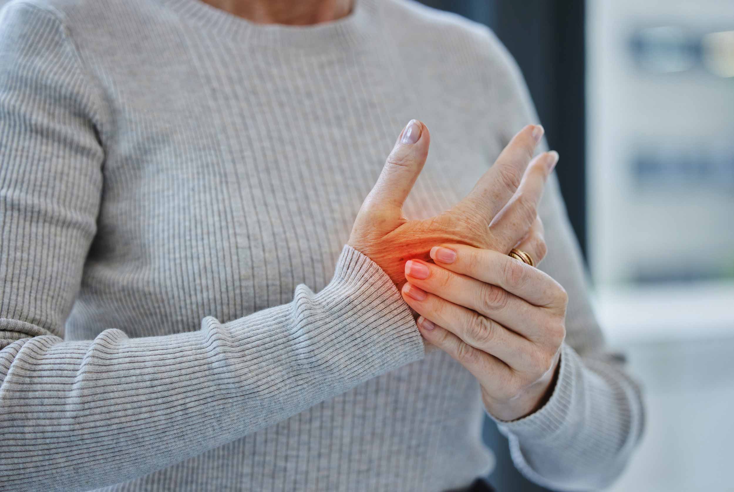 Schmerzen im Fingergelenk können ein Hinweis auf Arthritis sein Eine Frau hält sich ihre schmerzenden Finger