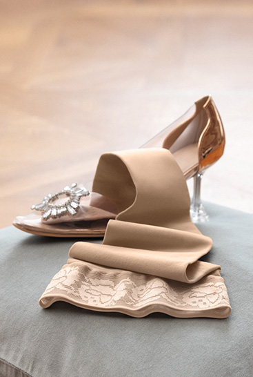 3. Lifestyle image Juzo Soft Juzo Soft Sesame lying on a cushion next to a Cinderella shoe