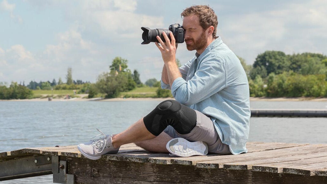 A photographer is sitting on a jetty. He is wearing a Juzo knee brace