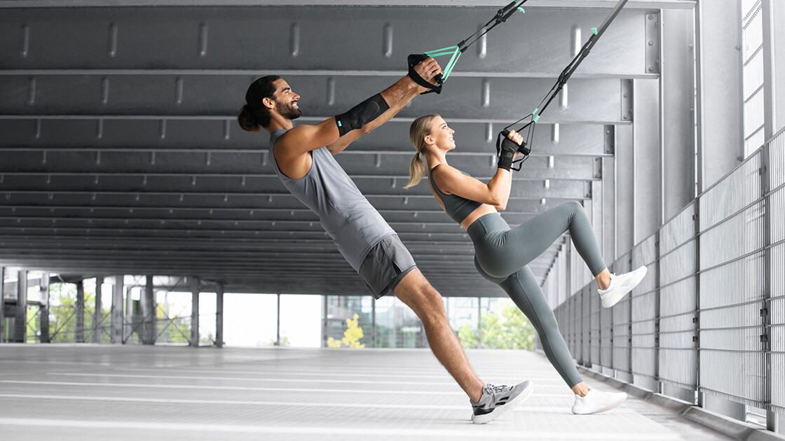 Um homem e uma mulher treinam numa garagem subterrânea com uma fita TRX Um homem e uma mulher treinam numa garagem subterrânea com uma fita TRX