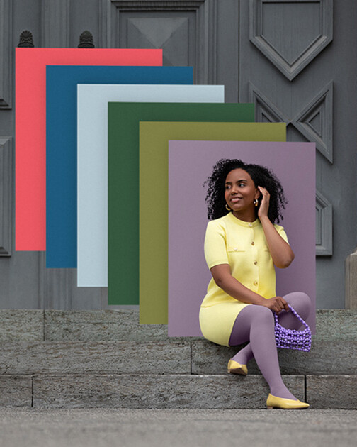 Frau mit Kompressionsstrümpfen in der Farbe Cozy Violet sitzt auf einer Treppe. Im Hintergrund die Farbfelder der aktuellen Juzo Trend Colours.