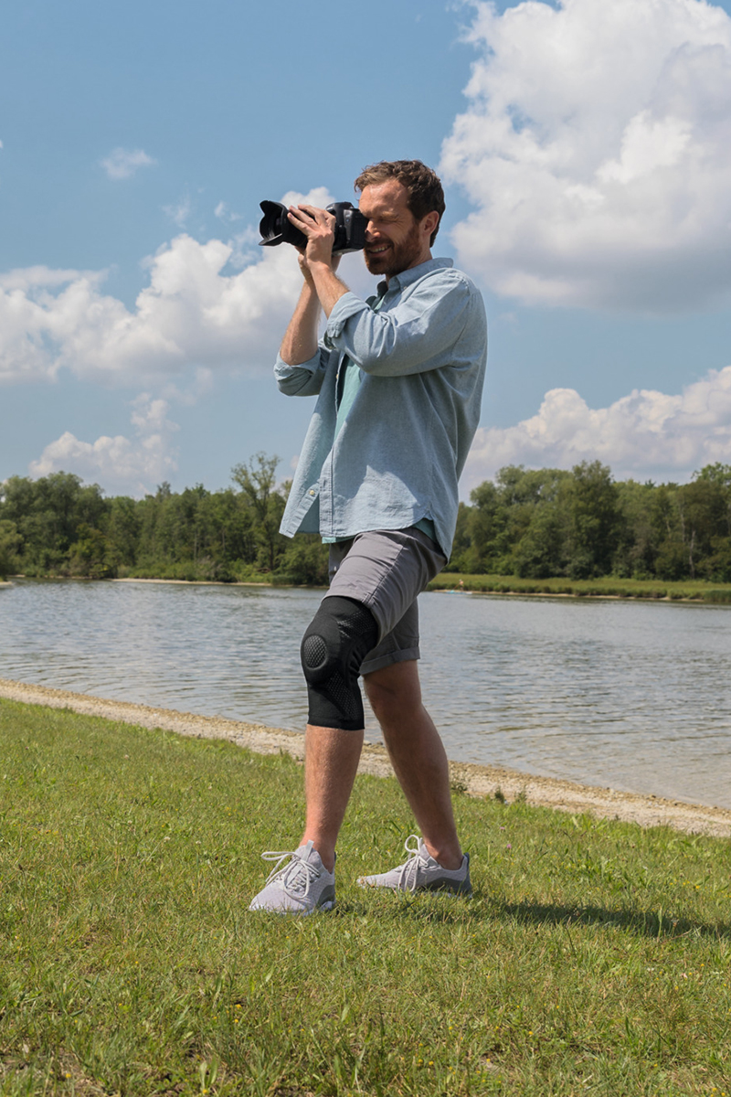A man is taking photographs in the countryside. He is wearing a knee brace. A man is taking photographs in the countryside. He is wearing a knee brace.
